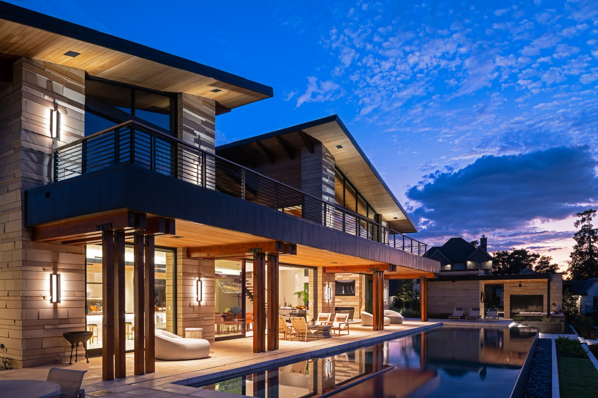 A finished Winn Wittman residence at dusk — modern volumes, deep overhangs, and a glass-walled great room over a reflecting pool.