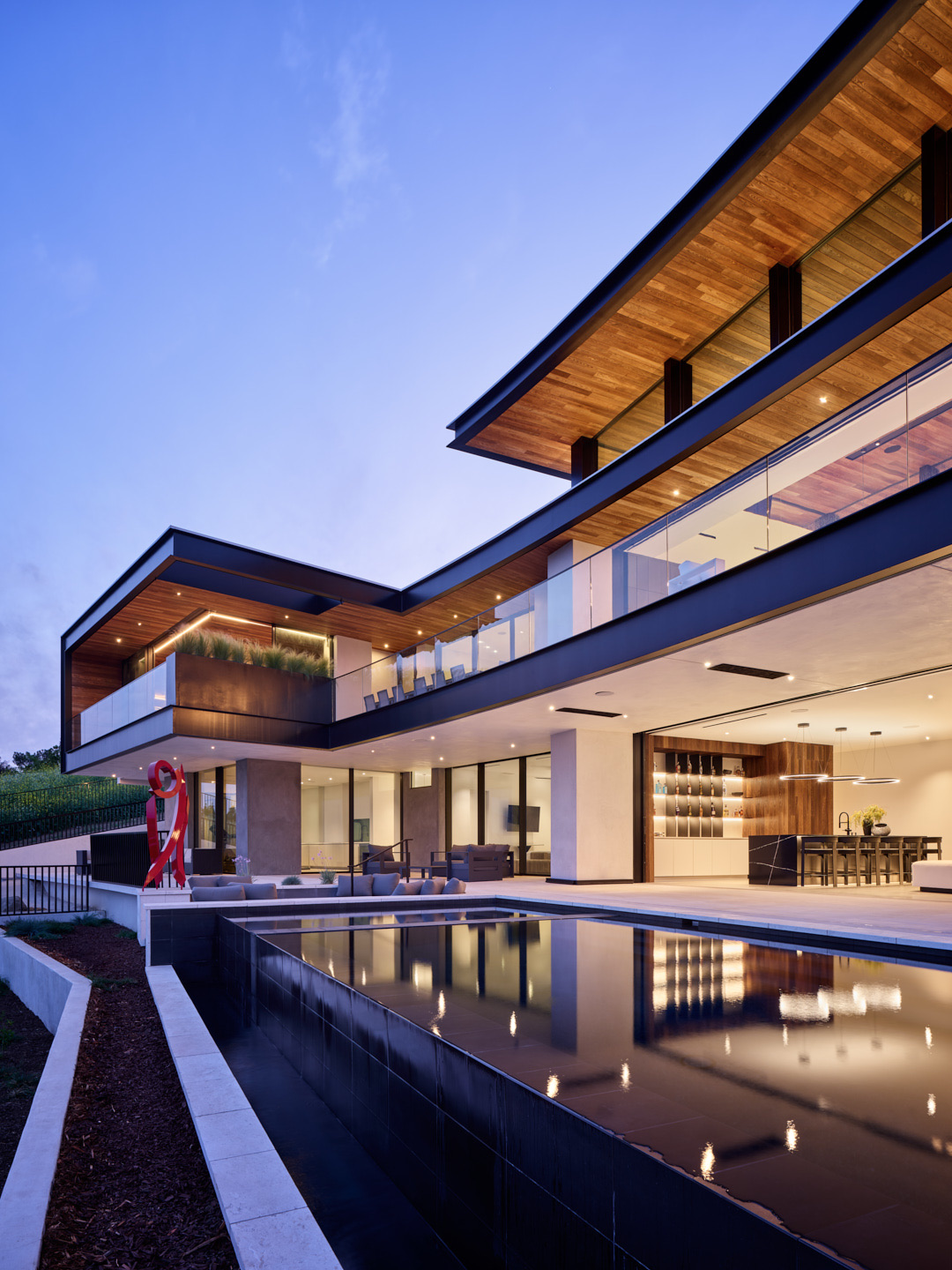 Modern residence at dusk with cantilevered volumes, glass walls, and a reflecting pool — a project realized from a consulting engagement.