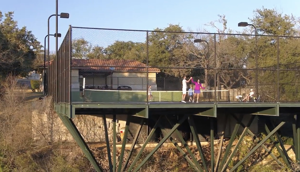 Players on an elevated steel-framed tennis court at dusk